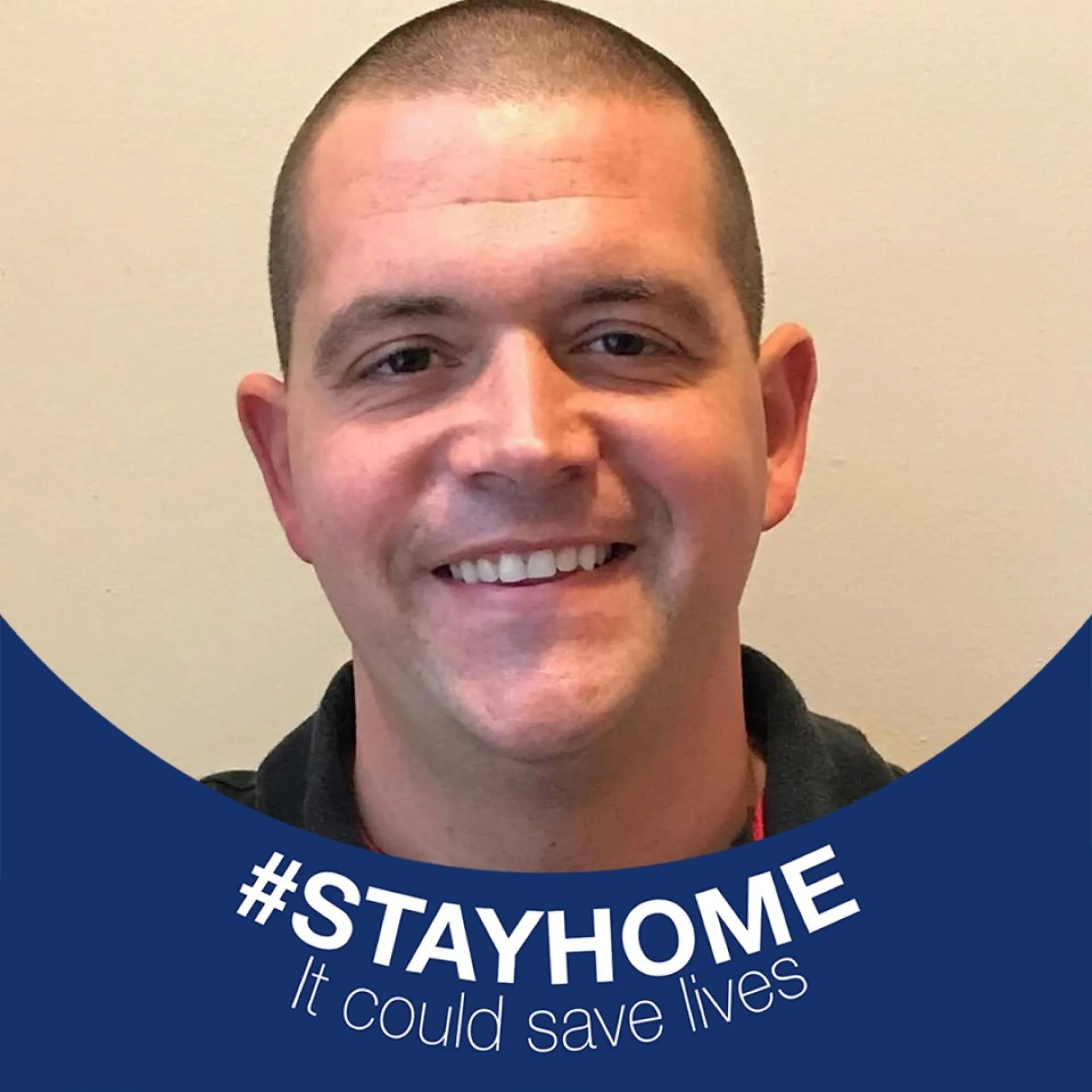 A man is smiling and wearing a #stayhome it could save lives sticker.